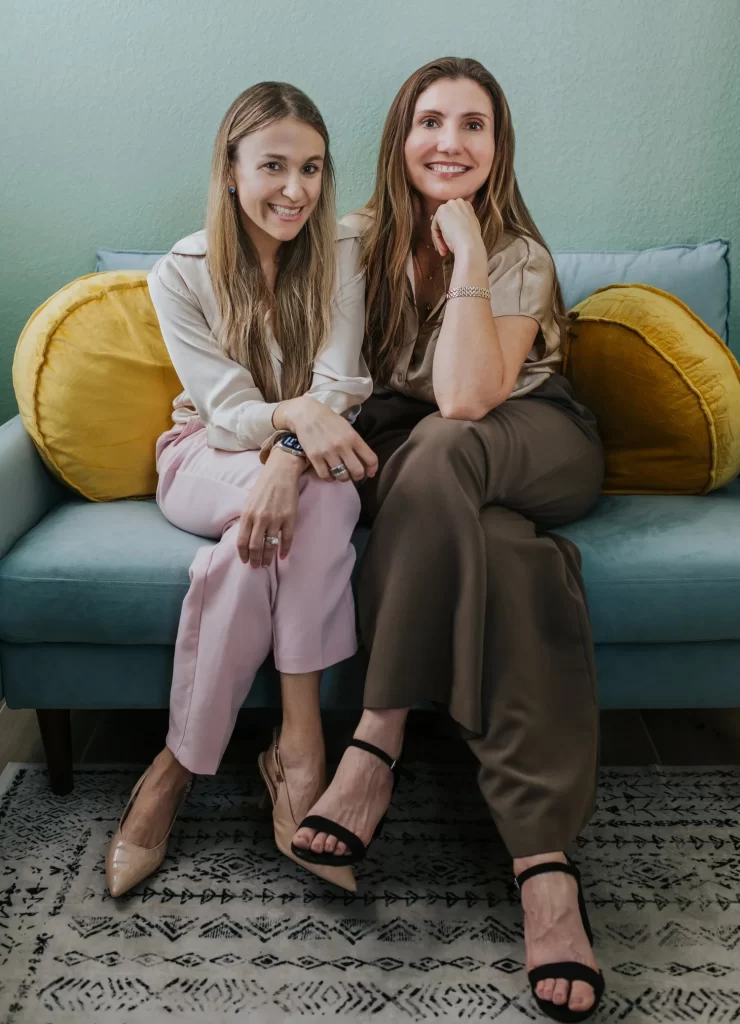 Dr. Allison Brazendale and Dr. Katrina Stone sitting together on a blue sofa